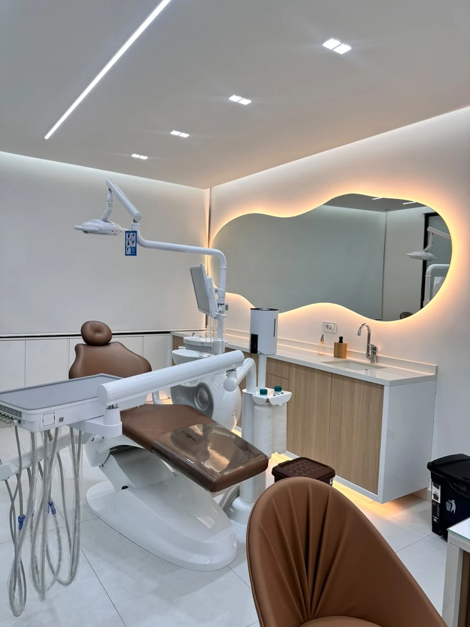 Treatment room with cognac dental chair, oak cabinetry and a warm backlit mirror